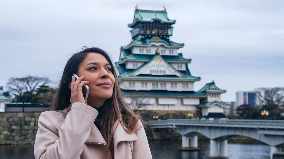 A woman on the phone with English-speaking customer support representatives while standing in front of Osaka Castle