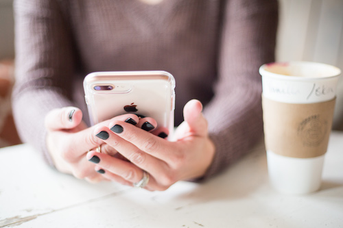 A woman is looking for something on her phone as she sits at a cafe in Kyoto with her coffee, enjoying the connectivity her travel SIM gives her.