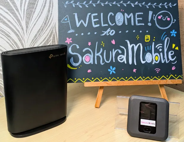 A fiber and Pocket WiFi device in front of a sign that reads "Welcome! to Sakura Mobile."
