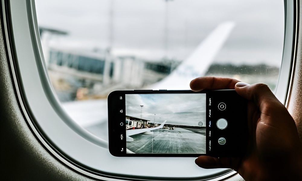 Hand holding phone taking photo of airplane wing and airport runway.