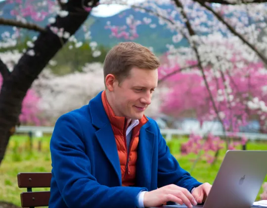 Man working on laptop with sakura trees in the background.