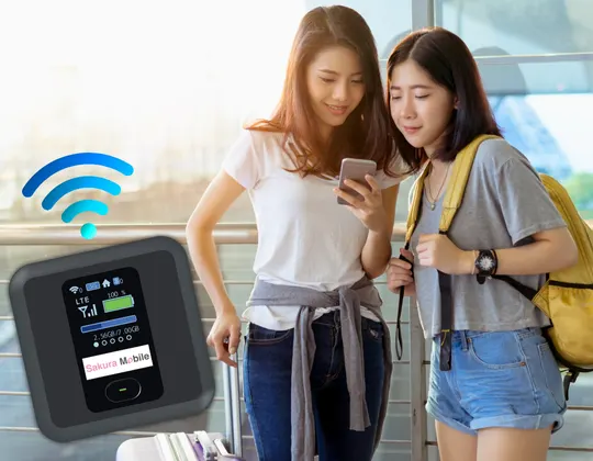 Two tourists that have just landed in Japan, looking at a phone while connected to a Sakura Mobile Pocket WiFi device.