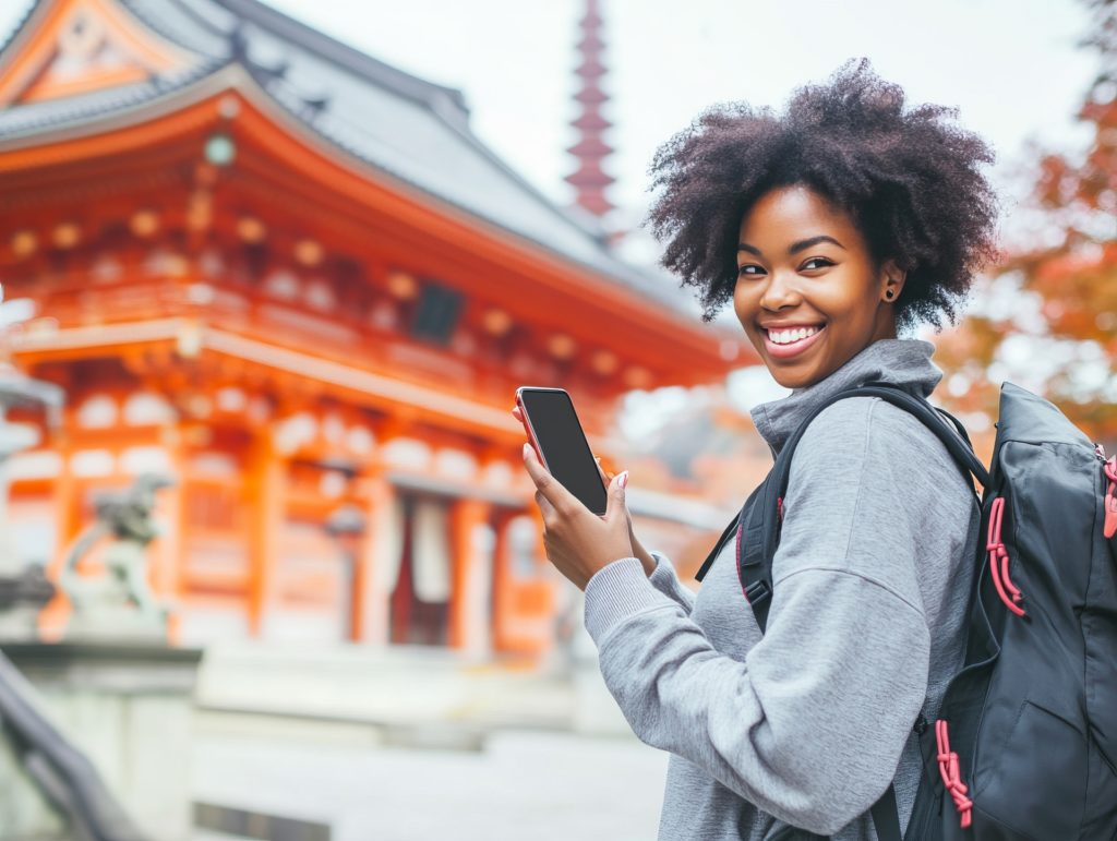 Cheerful young woman holding a smartphone in front of a Japanese Temple