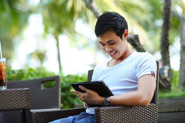 Man sitting outdoors, relaxing and using a tablet while enjoying a sunny day.