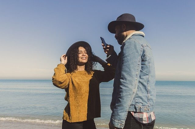 Couple taking photos with a smartphone on a sunny beach day.