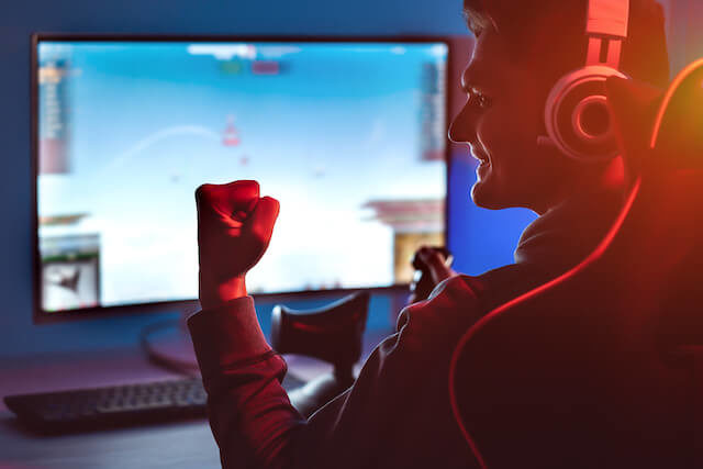 A game smiling and celebrating after fixing lag issues, enjoying smooth gameplay on a PC. The colorful lighting in the room reflects the excitement of a successful gaming experience.